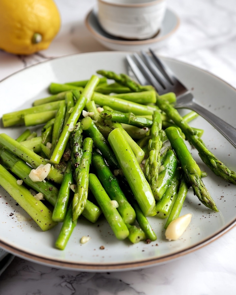 A close-up view of bright green asparagus cut into short pieces arranged in a single layer on a white plate with a thin brown rim, scattered with small bits of minced garlic and specks of black pepper for texture, a silver fork placed near the top edge of the plate, all set on a white marbled surface with a lemon blurred in the background. photo taken with an iphone --ar 4:5 --v 7