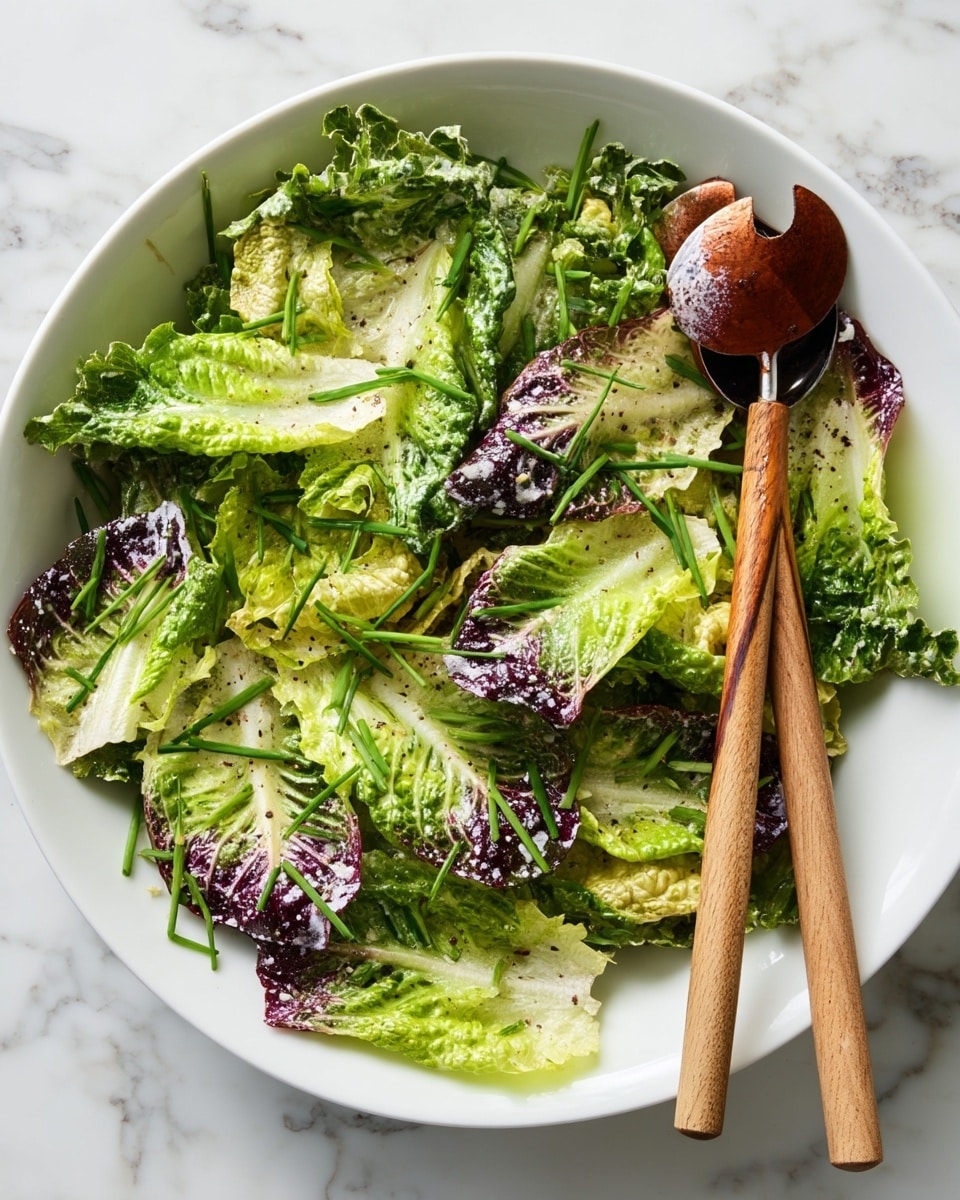 A fresh salad is shown in a large white bowl, with layers of green and purple lettuce leaves coated lightly with dressing. The leaves have a crisp texture with some bits of black pepper sprinkled on top. Scattered over the salad are thin, bright green chive pieces adding a fresh look. A pair of wooden-handled salad servers rest on the right side of the bowl. The whole scene is placed on a white marbled surface. photo taken with an iphone --ar 4:5 --v 7