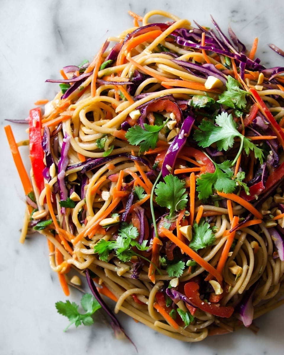 The dish is a colorful noodle salad with three main layers. The base layer is thick, light brown noodles that curve and twist throughout the plate. On top of the noodles is a mix of thinly sliced purple cabbage, thin orange carrot sticks, and bright red bell pepper strips, creating vibrant bursts of color. Scattered across the top are fresh green cilantro leaves and small pieces of chopped cashews, adding texture and a fresh look against the vegetables. The dish is presented on a white plate over a white marbled surface. photo taken with an iphone --ar 4:5 --v 7