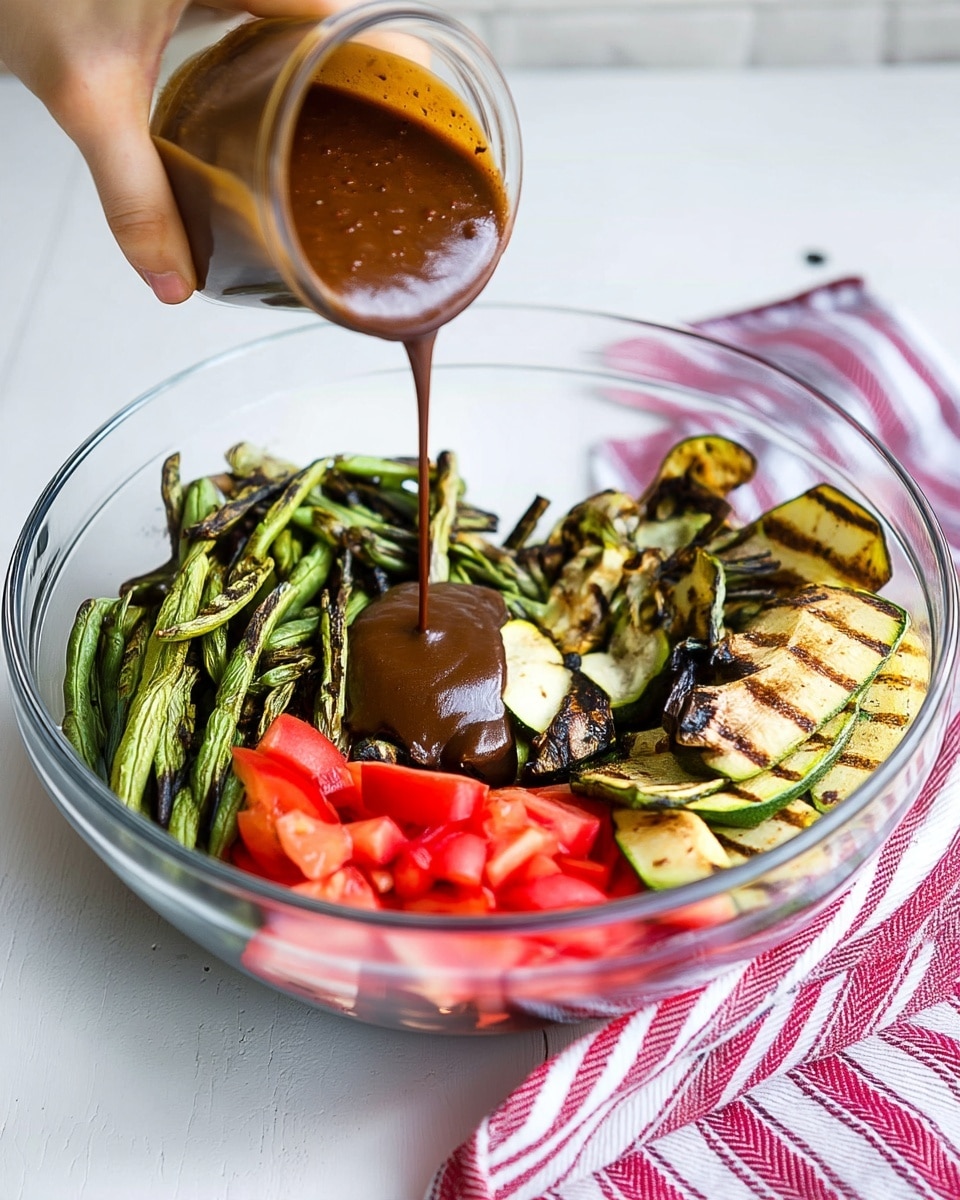 A clear glass bowl filled with four main layers of fresh ingredients placed on a white marbled surface. The bottom layer consists of bright red chopped tomatoes, positioned in the front. To the left and extending toward the back, there are grilled green beans with char marks giving a mix of light and dark green hues. On the right side, grilled zucchini slices with brown grilled marks show a creamy yellow and green mix. A thick dark brown sauce is being poured from a small clear glass jar by a woman's hand onto the center of the bowl, creating a smooth flowing line. A red and white striped kitchen cloth is placed near the bowl on the right side. Photo taken with an iphone --ar 4:5 --v 7