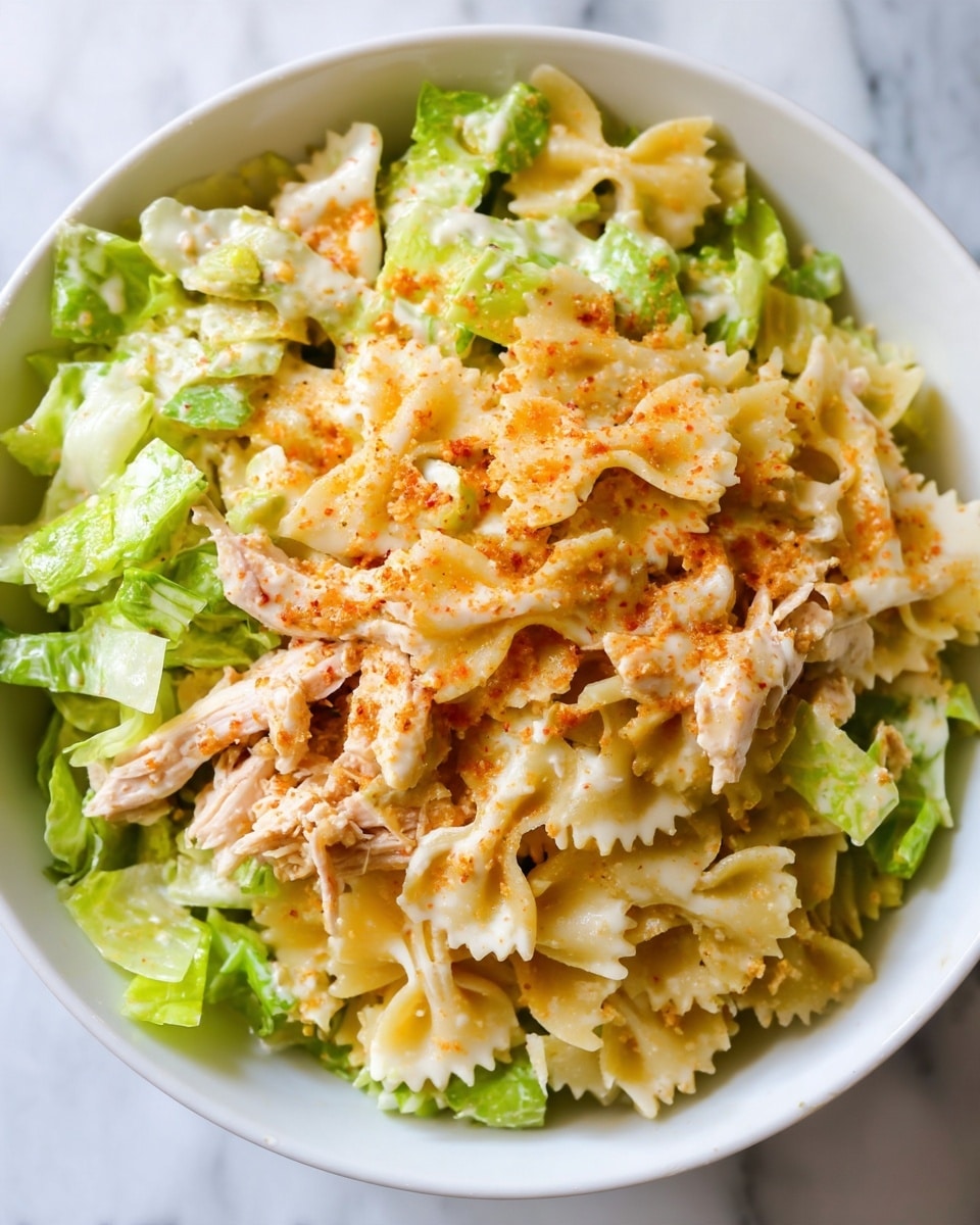 A close-up view of a salad served in a white bowl, showing three main layers: the bottom layer has light green chopped lettuce with a fresh, crisp texture; the middle layer consists of shredded pale beige chicken with a moist, fibrous appearance; the top layer includes light yellow bow-tie pasta mixed with a creamy white dressing that lightly coats the ingredients, sprinkled with a fine orange seasoning dust that adds contrast; all ingredients are mixed gently in the bowl, sitting on a white marbled surface. photo taken with an iphone --ar 4:5 --v 7